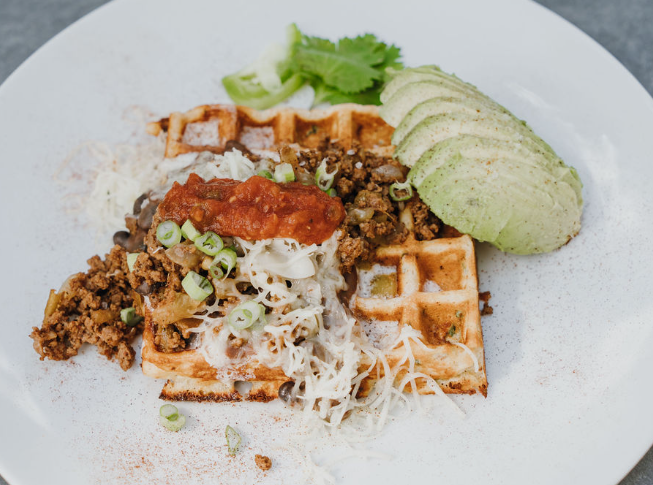 Savory jalapeño and cilantro Heavenly Waffles topped with ground beef, beans, melted cheese, and salsa, garnished with fresh cilantro.